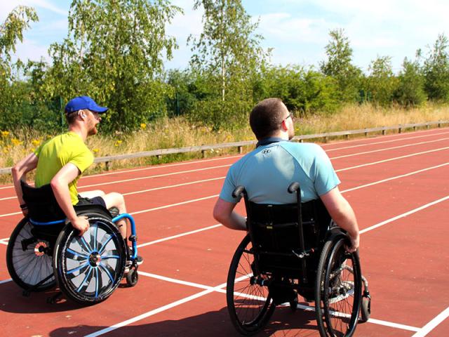 Two Treloar College students preparing to race on an outdoor sport track under a clear sky. It is a sunny and warm day. The boys are wearing T-shirts.