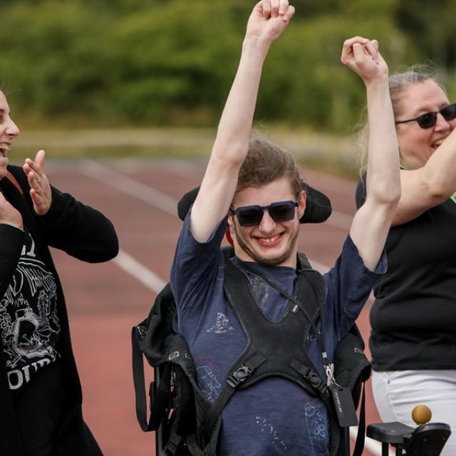 Treloar College student cheering on, raising his both arms up in the air - his 2 assistants are walking next to him and clapping. Everyone is having fun.