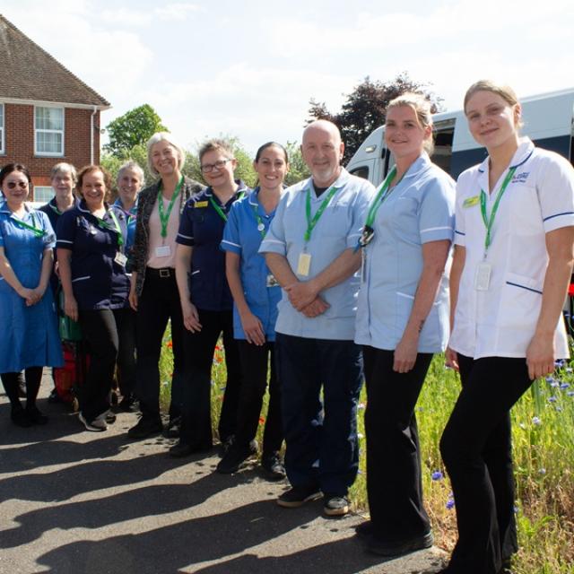 Treloar’s Nursing and Healthcare Team lined up outdoors posing for a group photo. It's a sunny day and behind them, there is a row of wild blue and red flowers.