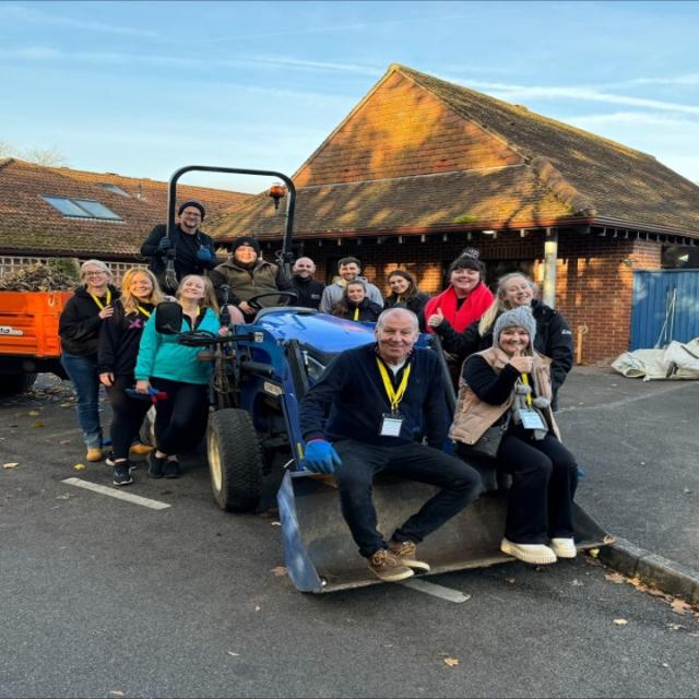 A group of volunteers gathered around a tractor, some of them sitting on it, some leaning against it. All looking at the camera and smiling.