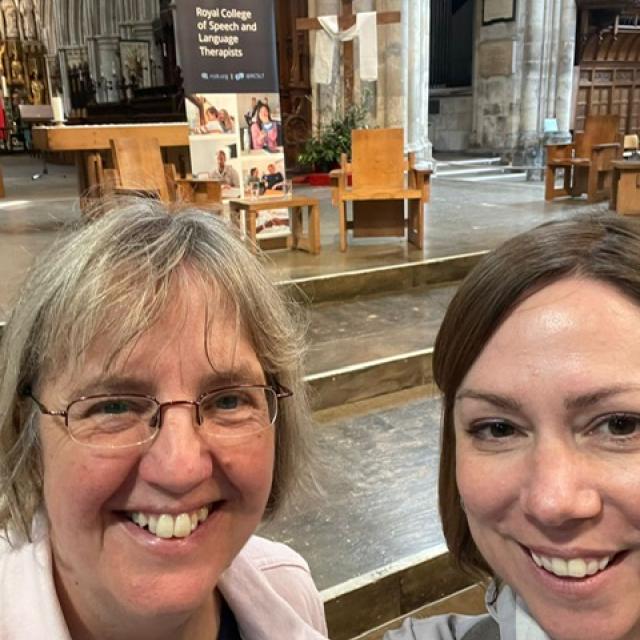 A selfie taken by 2 Treloar's Speech and Language Therapists, Emily Ball and Caroline Weighton, at a special non-denominational Anniversary event at Southwark Cathedral. A banner of the event in the background. Emily and Caroline are smiling to the camera. 