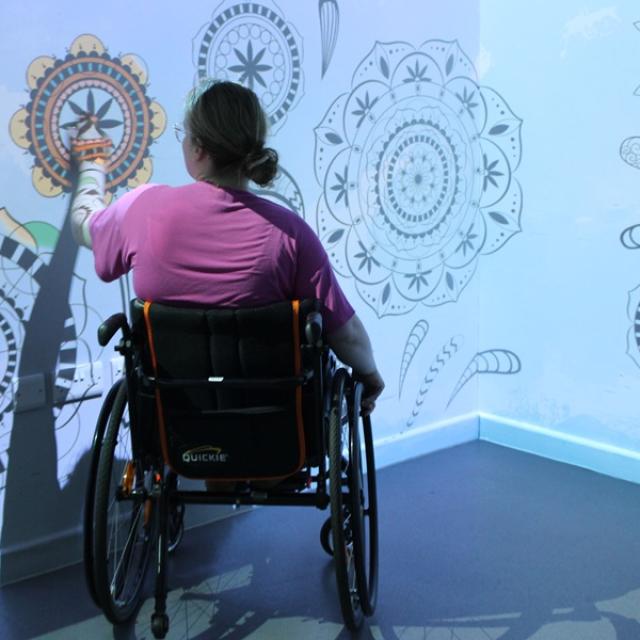 Treloar College student wearing a pink shirt and is interacting with intricate black and white mandala designs projected on the wall.