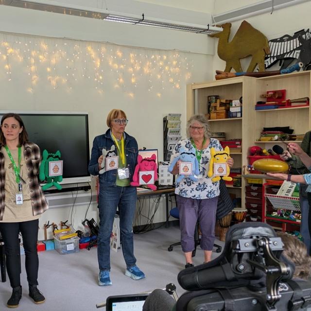 Philippa Perry from BBC Radio 3 with Treloar's staff members during a music lesson: they are all standing in front of the class, holding toys with attached stickers portraying different emotions.