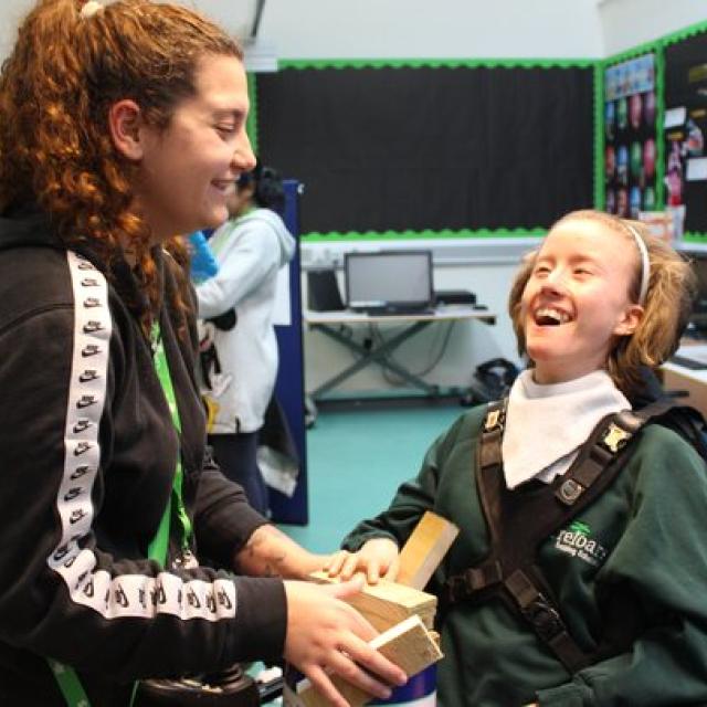 student smiling with support assistant, using bricks to balance