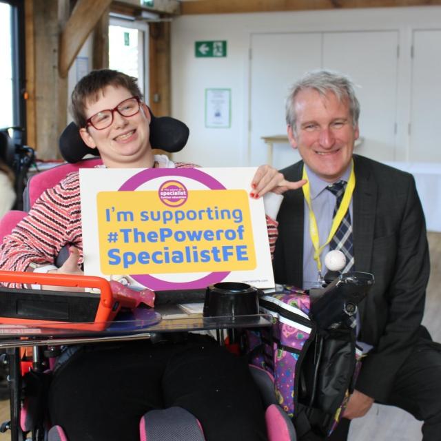 Damian Hinds MP for East Hampshire is seated side by side with Treloar College student, who is holding  up a pledge board which says 'I'm supporting The Power of Specialist FE'
