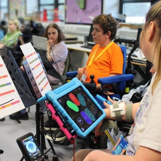Treloar's student using a tablet to play the clarion in a classroom setting with music sheets on stands nearby.
