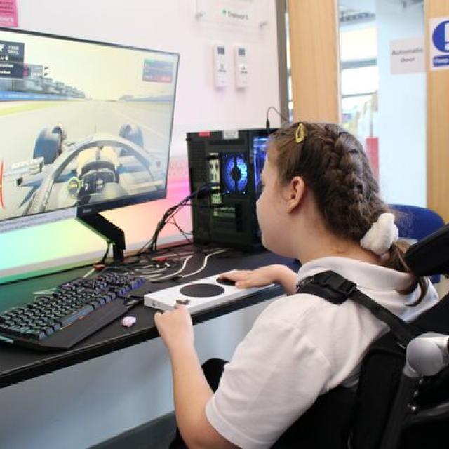 Treloar's student playing a racing video game on a desktop computer with a large monitor in a bright room.