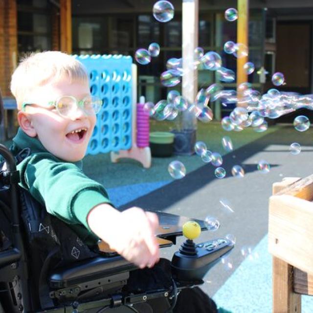 Treloar's primary student joyfully reaching out to catch floating soap bubbles outdoors on a sunny day.