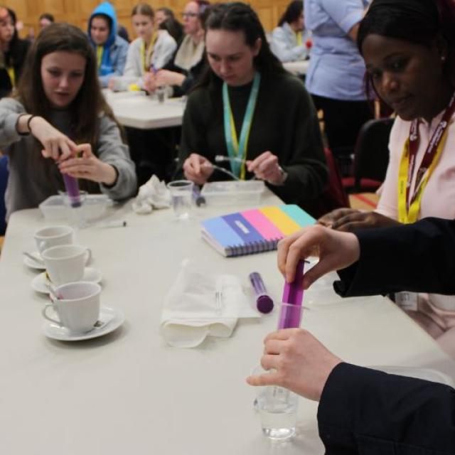 Group of first-year nurses around a table engaging in a hands-on activity with test tubes and notebooks in a classroom setting.
