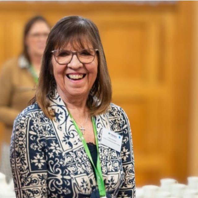 Photo of Cheryl Brewer Chair of Trustees Treloar Trust, she is wearing a blazer and a green lanyard, smiling towards the camera