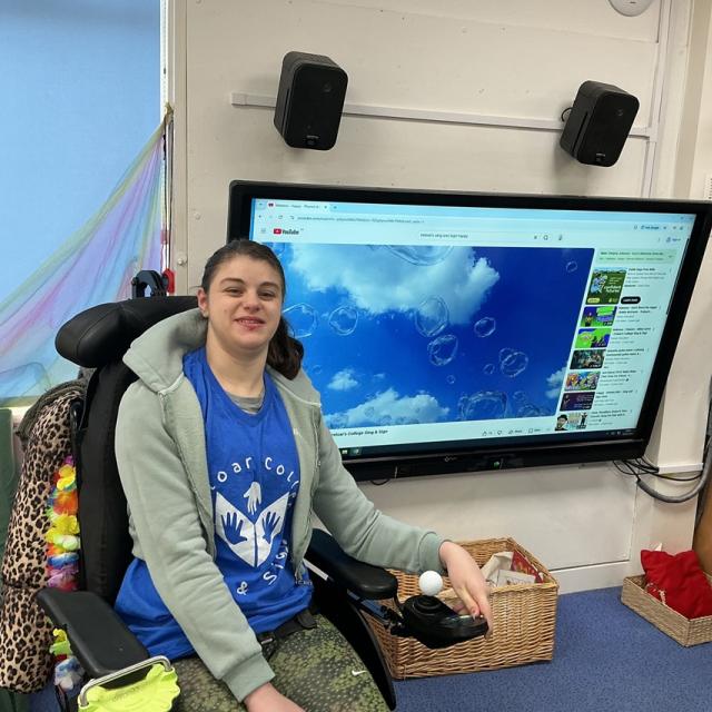 Treloar College student in front of a large screen displaying a YouTube video of bubbles against a blue sky.