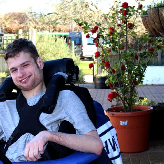 Treloar College student outdoors near a potted rose bush on a sunny day. He is smiling and posing for a photo.