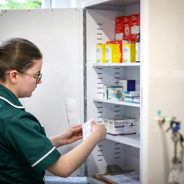 Treloar's medicine management technician, stands in front of a cabinet of medication, checking a label on a packet.