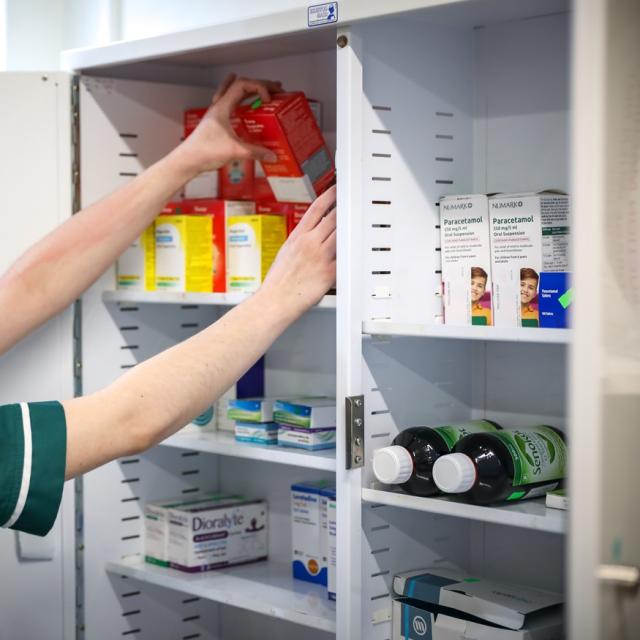 Pharmacist organizing various medication boxes and bottles inside a white medicine cabinet.