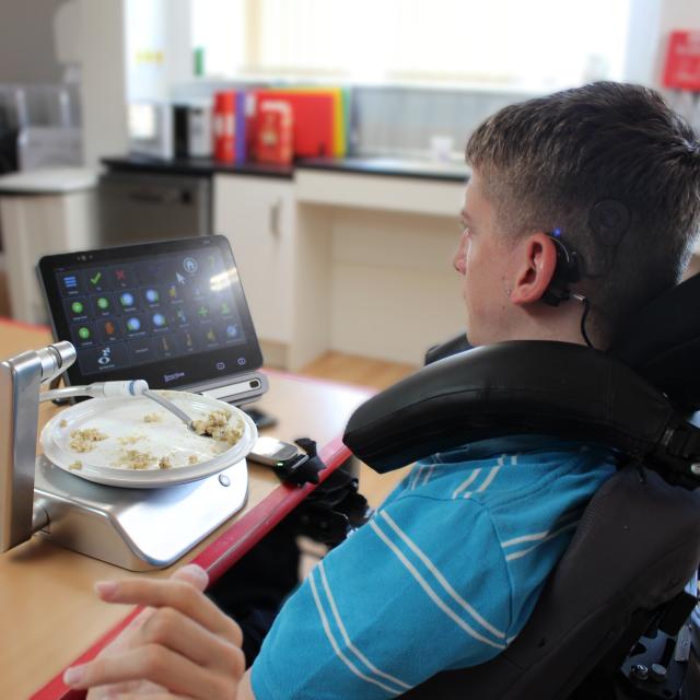 Student using eye gaze control via an AAC to operate a neater eater adaptable feeding system