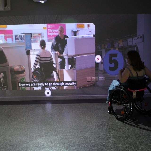 Treloar College student watching a video projected on a wall showing airport security screening with subtitles.