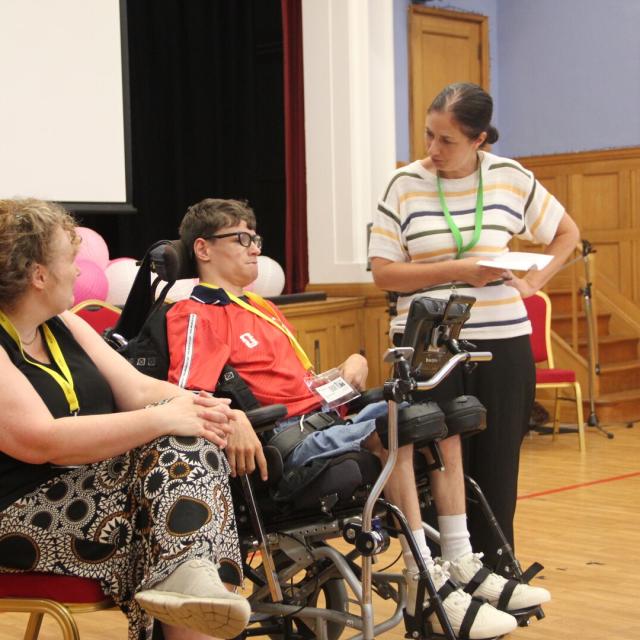 Student in a wheelchair speaks with staff member in School hall