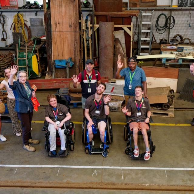 A group of students in wheelchairs in a heritage railway workshop, with an outline of a carriage marked out on the floor