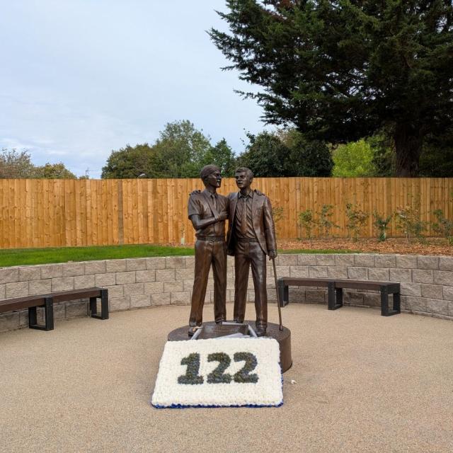 Treloar's Memorial to students affected by infected blood, a bronze statue of two boys, with a floral tribute at the base, in memory of the students who died following the treatment they received.