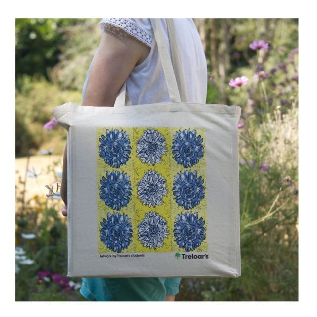 Canvas tote bag with a grid of blue floral designs on a yellow background, held by a person outdoors.
