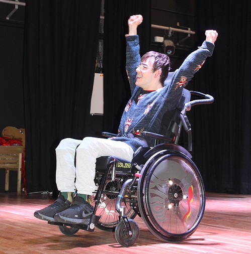 Student on a stage, raising his arms in the air in celebration