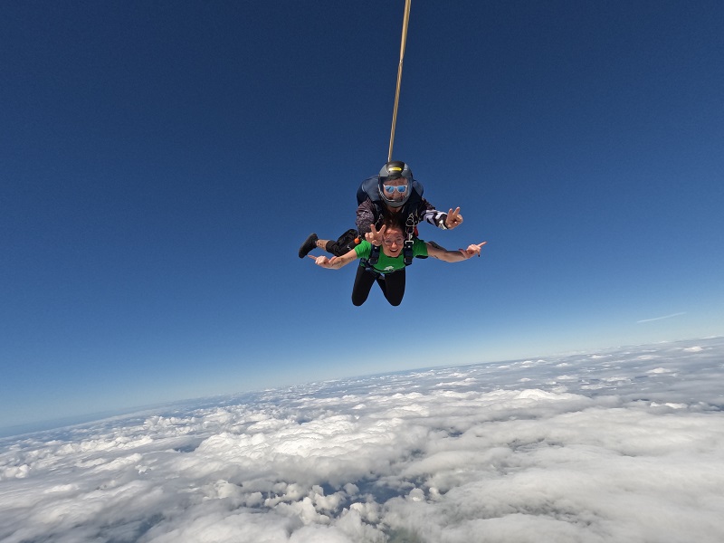 Treloar's staff member up in the sky above clouds skydiving while strapped to the instructor