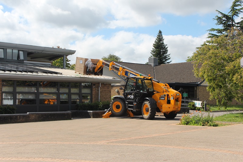 An orange JCB using its crane to place solar panels on the roof of Treloar's building