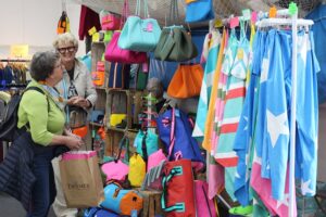 One of the stallholders chatting with a guest and laughing. The stall is full of bright, colourful swimming gear