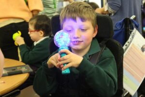 Treloar's student holding an illuminated, microphone-line objects close to his face, looking at its bright light
