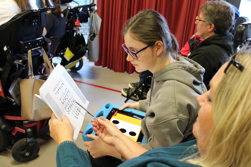 In assembly, Treloar School student is looking at a braille book together with her support assistant