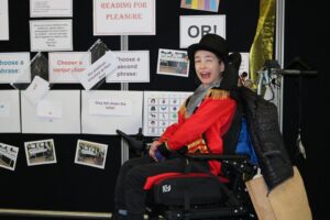 Student in a fancy dress costume with a  top hat, smiling in front of a World Book Day display