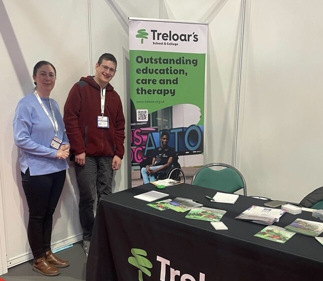 Maria Sherwood, Treloar's Progress and Transition Team Manager at Naidex with former student Eoin standing by Treloar's exhibition stand with branded merchandise.