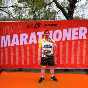 Treloar's supporter Andrew posing for a photo after the marathon; a big red banner saying 'marathoner' behind him.