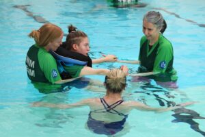 Suzanna Hext in the pool talking to 2 assistants who are supporting Treloar's student with swimming exercises