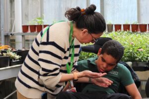 Student support assistant is letting primary student smell and see a mint leaf that she has in the palm of her hand 