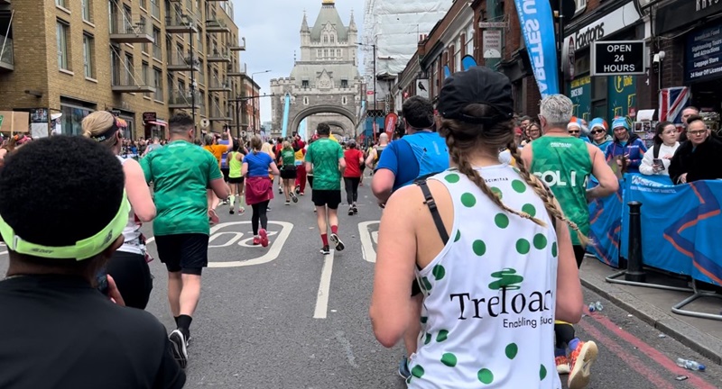 One of Treloar's supporters running in the London Marathon: we can see the back of her Treloar's branded vest which is white with green dots and Treloar's logo in the middle