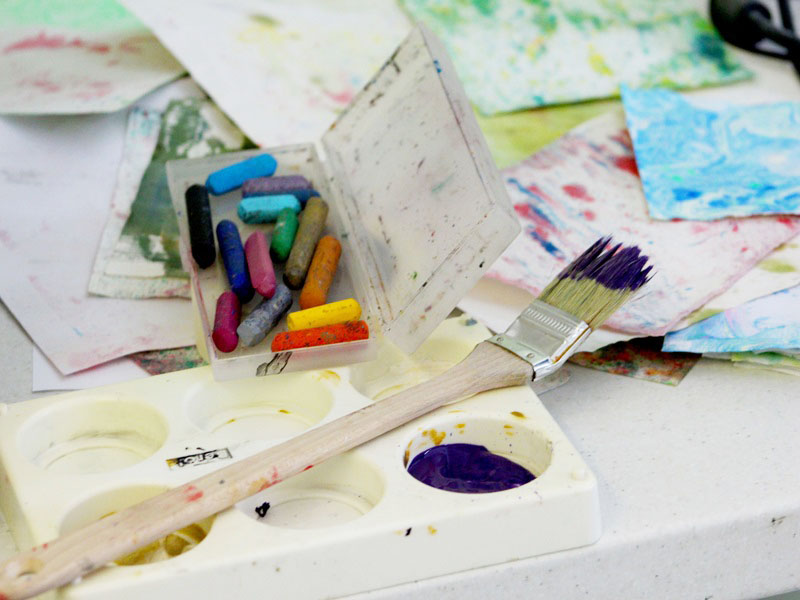 Paint brush, crayons, paints and artworks on the table